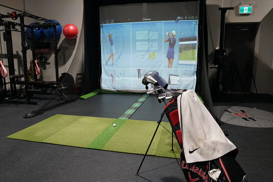 Indoor golf simulator with swing analysis screen, hitting mat and golf bag in a sports rehabilitation space