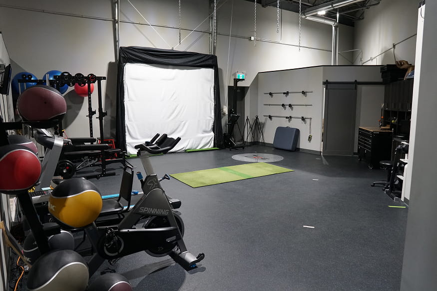 Rehabilitation and training area with exercise bikes, medicine balls, strength equipment and a golf simulator screen