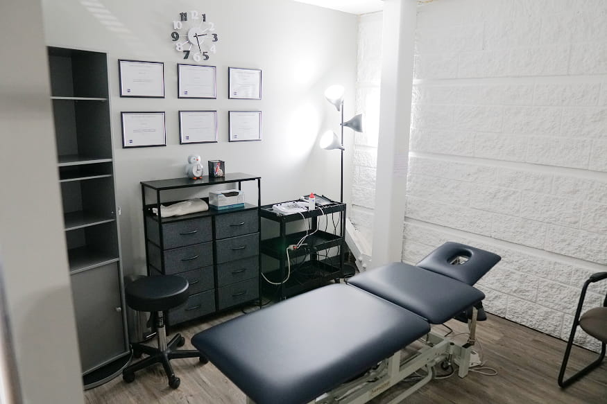 Private treatment room with an adjustable treatment table and framed practitioner credentials on the wall